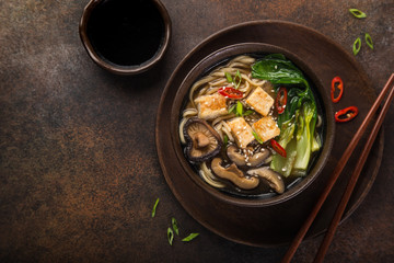 asian vegan noodle soup with tofu cheese, shiitake mushroms and pak choi, dark background