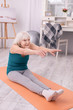 © Viacheslav Yakobchuk - Nice warmup. Upbeat senior woman sitting on the yoga mat and stretching herself before working out in the morning
