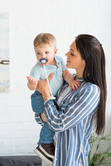 portrait of young mother and little baby with pacifier at home