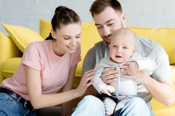 Wall Mural - smiling parents with son sitting on yellow sofa