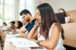 © serhiibobyk - Sideview of young student prepearing for exams in university.Girl sitting on wooden desk in spacy modern university classroom with big panoramic windows. Working with project.