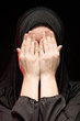 © Ivan Traimak - Portrait of beautiful serious young muslim woman wearing black hijab with hands near her face as praying concept on black background