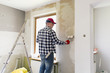 © artursfoto - Glueing wallpapers at home. Young man, worker is putting up wallpapers on the wall. Home renovation concept