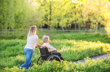 Elderly grandmother in wheelchair with granddaughter in spring nature.