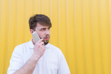 Wall Mural - A serious man speaks by telephone on the background of a yellow wall and looks aside. Serious conversation on the phone