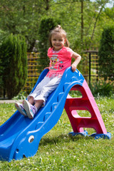 A child enjoys a blue hair on a sunny day, playful in the yard, on the grass, descends down the slide