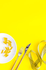 Wall Mural - Dietary supplement for well-being. Fish oil or omega-3 capsules on plate near measuring tape on yellow background top view copy space