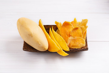 Dehydrated mango slices and fresh raw mango on wooden plate on white table. Dried fruits. Natural healthy candy.