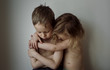 © Cavan Images - Shirtless sister embracing sad brother by wall at home