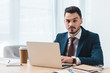 © LIGHTFIELD STUDIOS - handsome young businessman using laptop and looking at camera in office
