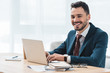 © LIGHTFIELD STUDIOS - handsome young businessman using laptop and smiling at camera in office