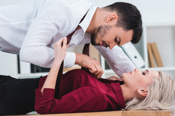 side view of businessman unbuttoning shirt of young businesswoman at workplace