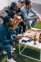 Wall Mural - high angle view of multiethnic friends eating pizza and watching american football match