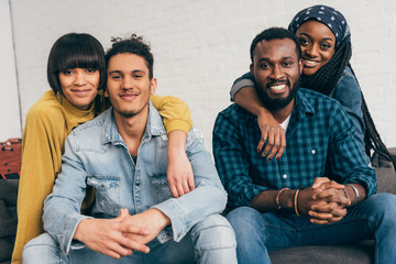 Wall Mural - two young smiling couples sitting on couch and looking at camera