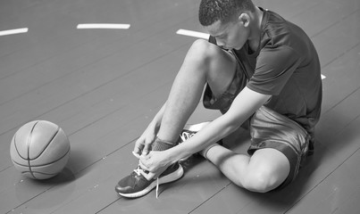 Wall Mural - African American teenage boy tying his shoe laces on a basketball court