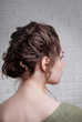 © pushann - Hairstyle of a high bun on the head of a brown-haired close-up of a rear view against a white brick wall.