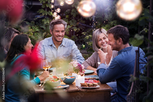 Fotomural Group of friends gathered around a table in a garden on a summer evening to shar