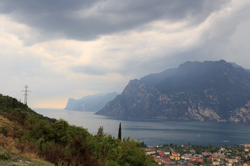 Panorama of Lake Garda, lakeside village Torbole and mountains with dark storm clouds, Italy