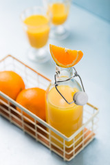 Glass of fresh orange juice with orange slices on white plate, blue background, cold summer refreshing nutritional beverage, blue orange color contrast, vitamin C healthy drink, copy space