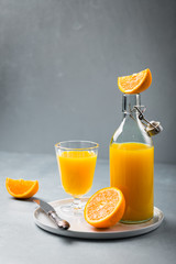 Glass of fresh orange juice with orange slices on white plate, blue background, cold summer refreshing nutritional beverage, blue orange color contrast, vitamin C healthy drink, copy space