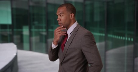 Wall Mural - Smart African corporate employee thinking up a solution to a financial issue in the lobby of a business building, Young African-American businessperson thinking to himself at work, 4k