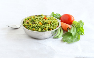 Wall Mural - Palak rice, biryani or pilaf, which is made from spinach and vegetables like tomato, carrot and long green beans, is an Indian vegetarian healthy food, in a steel bowl.