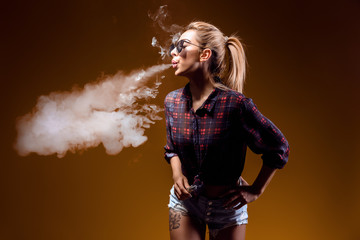 Attractive glamour woman standing and vaping on yellow background.