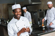 © LIGHTFIELD STUDIOS - smiling african american chef using smartphone at restaurant kitchen and looking at camera