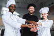 © LIGHTFIELD STUDIOS - smiling multicultural chefs putting hands together at restaurant kitchen