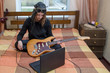 © Pavlo - The girl connects the electric guitar to the laptop sitting on the bed