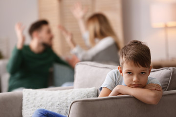 Wall Mural - Little unhappy boy sitting in armchair while parents arguing at home