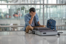 Traveller Man In Casual Clothes  Sitting Behind His Unpack Luggage  And Use Hand Touch Head With Unhappy Because Passport Lost At The Terminal Airport.