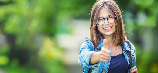 Wall Mural - Attractive young teenage schoolgirl showing thumbs up