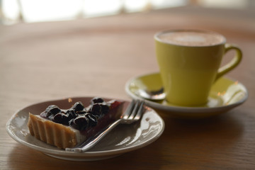 Wall Mural - Cup of cappuccino coffee and blueberry cheese pie on table in cafe