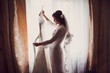 © VlaDee - Beauty bride is holding her dress near window in the morning