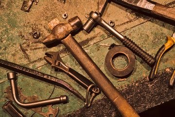 Still life of old hand tools. On the dirty table lie a hammer, electrical tape, wrench, pliers, nut, and other tools.