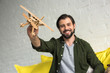 © LIGHTFIELD STUDIOS - close-up view of happy young man playing with wooden toy plane and smiling at camera