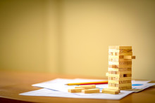 Blank Wooden Block Leaning On A Structure Made Of Many Other Blocks With Several Of Them Still Lying Scattered On A Textured Rustic Wooden Desk. Conceptual Of Leisure Game Or Start Up Business