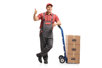 Wall Mural - Mover leaning on a hand truck loaded with boxes making a thumb up gesture