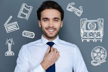 Famous actor. Cheerful successful famous actor smiling and touching his tie while getting ready for a fashionable party