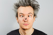 © vika33 - Unshorn and unshaven squint young guy with piercings on his face, with a fly on the nose, on gray background.