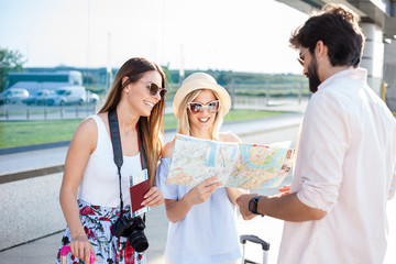 Young man giving directions to two beautiful young female tourists. Standing in front of the airport terminal building with suitcases, maps, passports and camera.