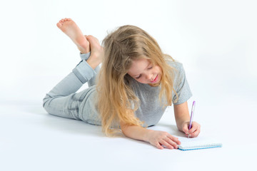 Beautiful little girl lying down writing on a blank sheet in a notebook.