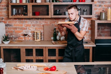 Wall Mural - Young unskilled cooker scrutinizing self-cooked pizza. Homemade food, cooking man, people concept