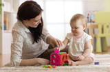 Fototapeta  - Babysitter and one year old baby playing with toys in nursery