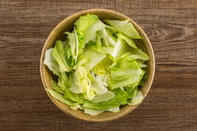 Iceberg Lettuce Table Top Fresh Torn Salad Leaves In A Wooden Bowl Isolated On Brown Wood Background.