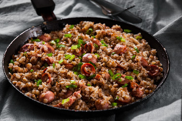 Wall Mural - Fried Meat sausages in a frying pan with buckwheat porridge on dark wooden table