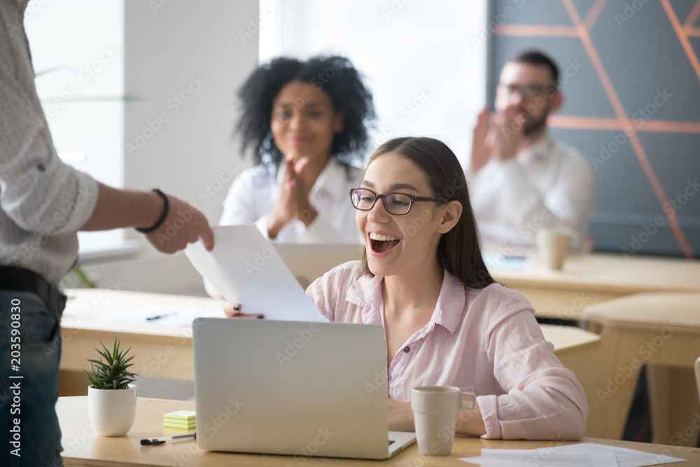 Excited successful student receiving document from boss with good result, colleagues congratulating happy millennial promoted rewarded employee amazed by great news in written notice with applause - obrazy, fototapety, plakaty 