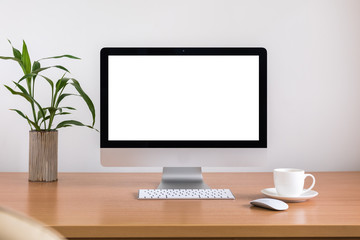 All in one computer, mouse, keyboard, coffee cup and plant vase  on wooden table