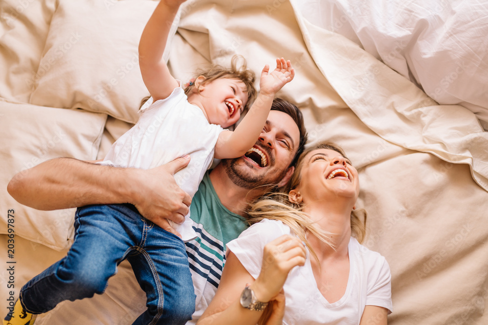Happy family having fun in the bedroom while they lie on bed - obrazy, fototapety, plakaty 